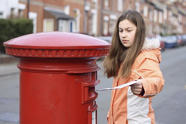 A woman posting a letter into a post box.