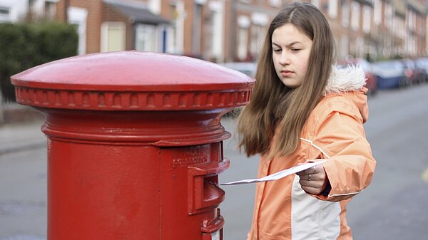 A woman posting a letter into a post box.